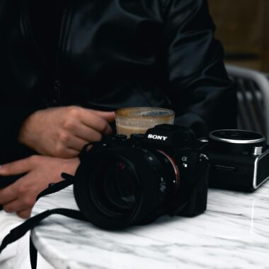A man in a leather jacket drinks coffee at a caf&eacute; in Ankara with a camera on the table.