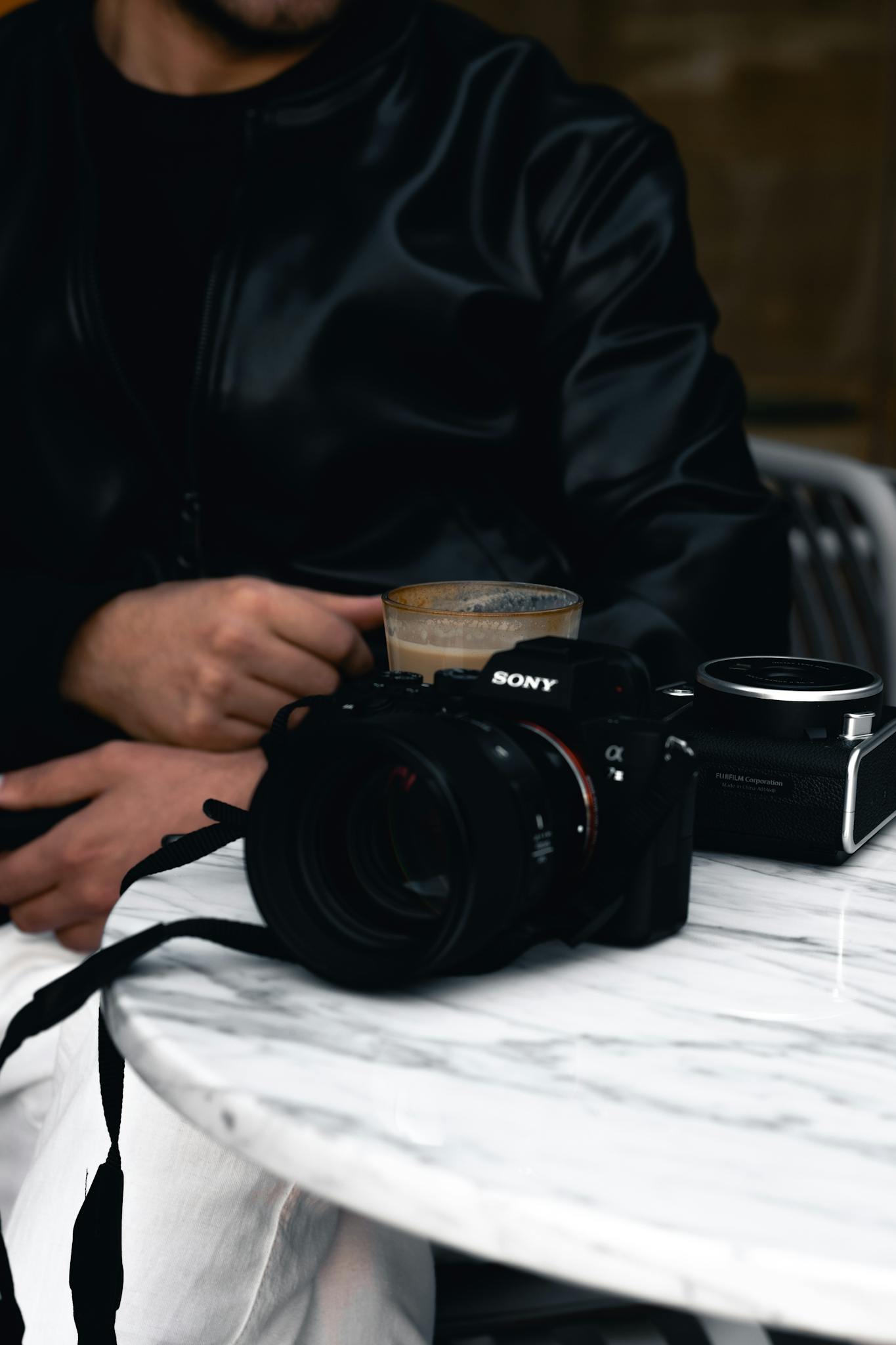 A man in a leather jacket drinks coffee at a caf&eacute; in Ankara with a camera on the table.