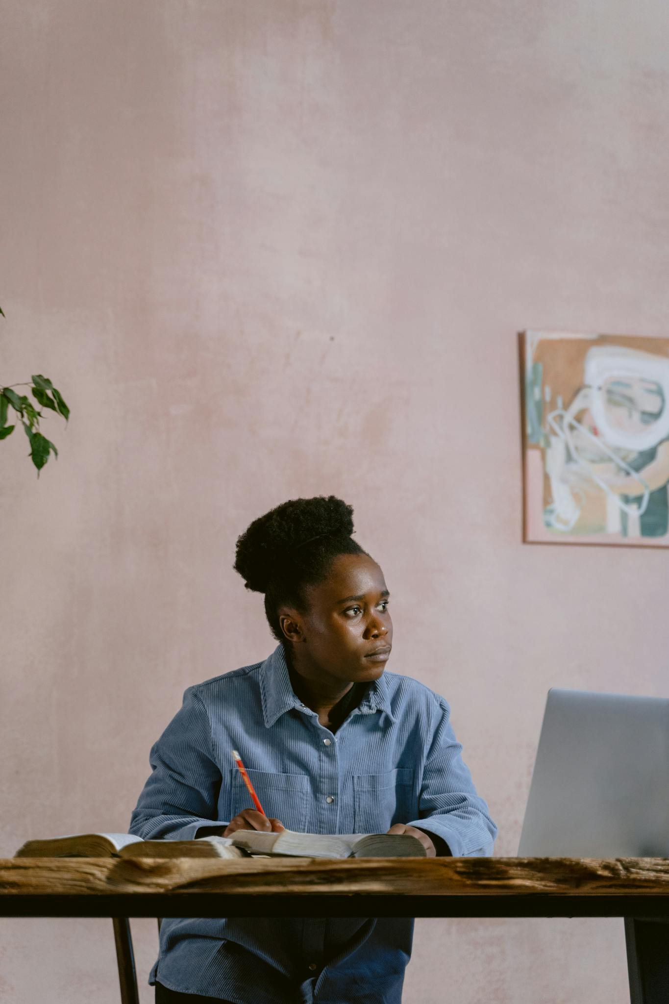 An adult working intently at a desk in a home setting, surrounded by books and art.