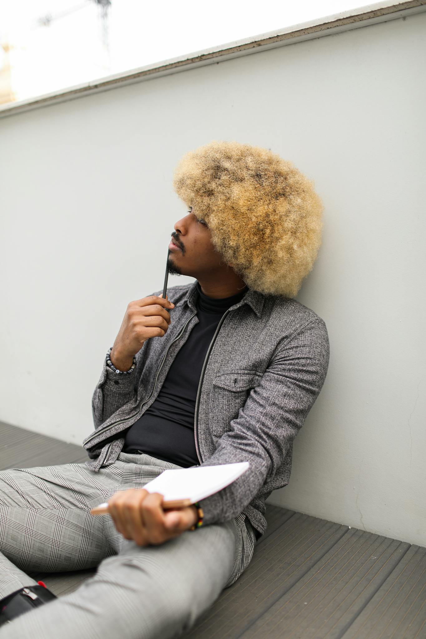Man with an afro hairstyle sitting and pondering with a notepad and pen.