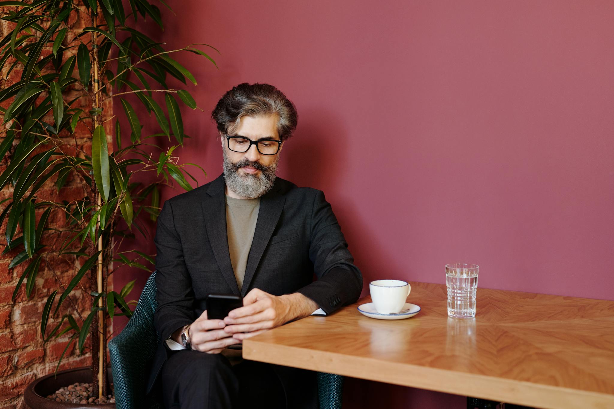Stylish bearded man sitting in cafe using a smartphone with a cup of coffee.