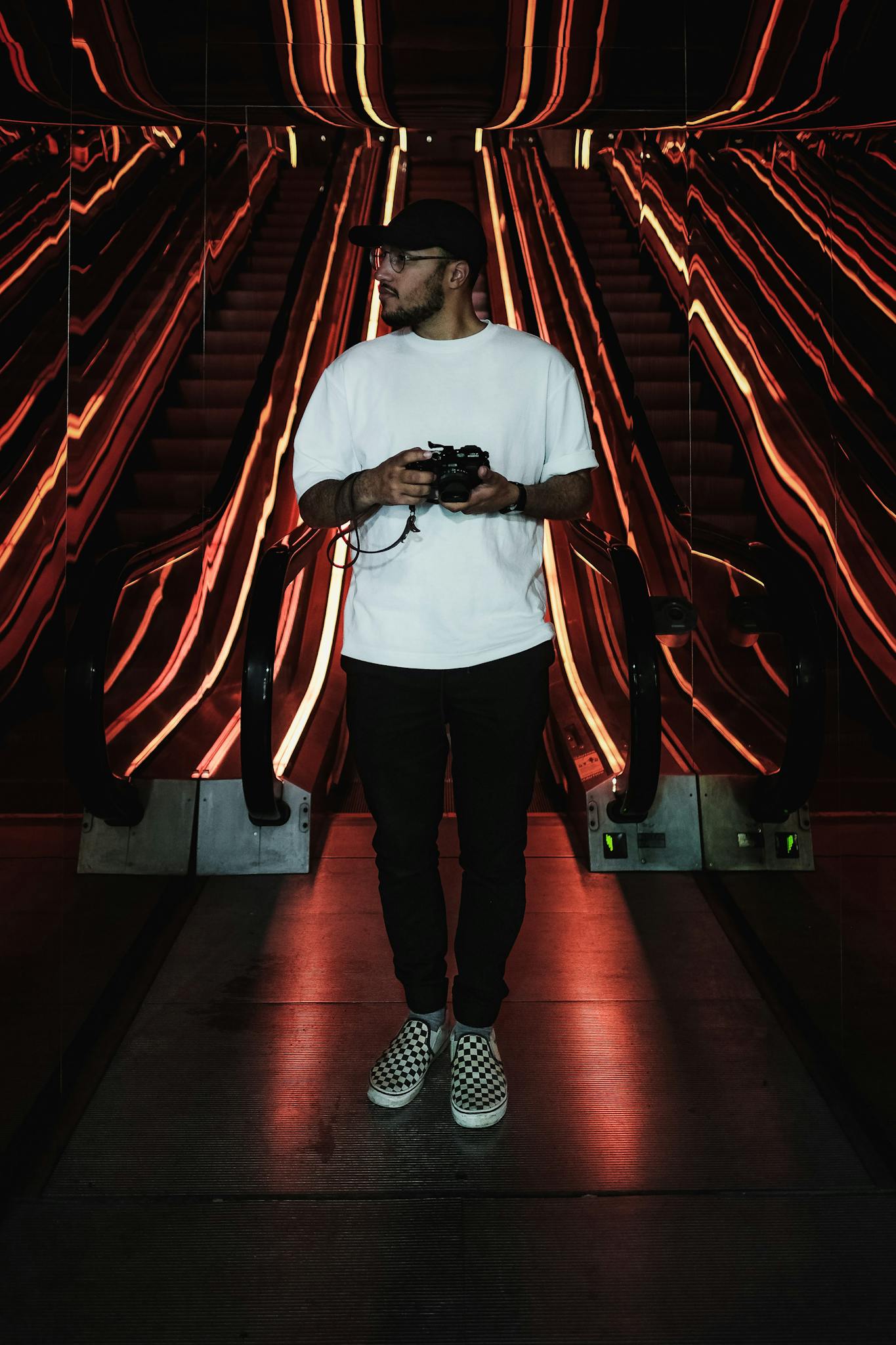 Young man holding camera amidst futuristic escalator lights in New York.